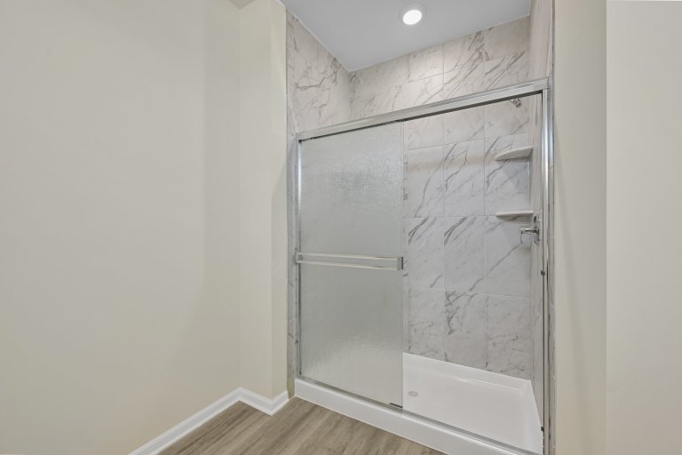 Walk-in shower with glass enclosure and built-in wall shelving in a new construction primary bathroom.