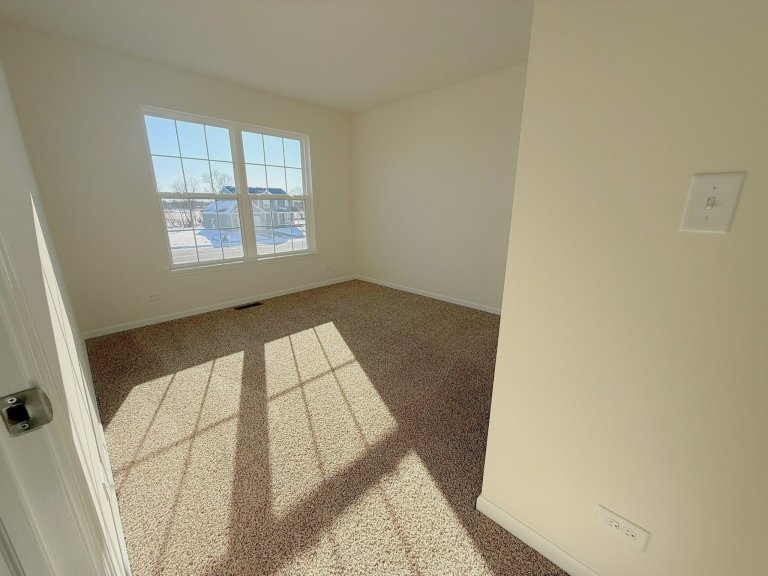 Secondary bedroom in Georgian floor plan featuring large window, natural light, neutral carpet, and bright layout in a new construction home.