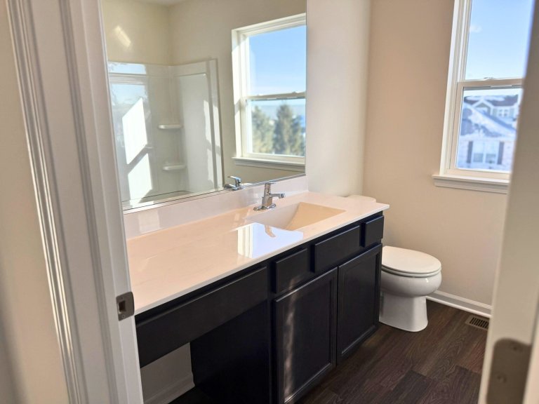 Bright new construction bathroom showcasing large mirror, modern vanity storage, and natural light window.”