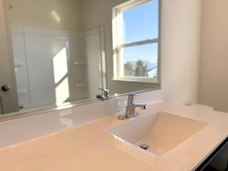 Modern bathroom vanity in Georgian floor plan featuring white countertop, undermount sink, chrome faucet, and natural light window in a new construction home.