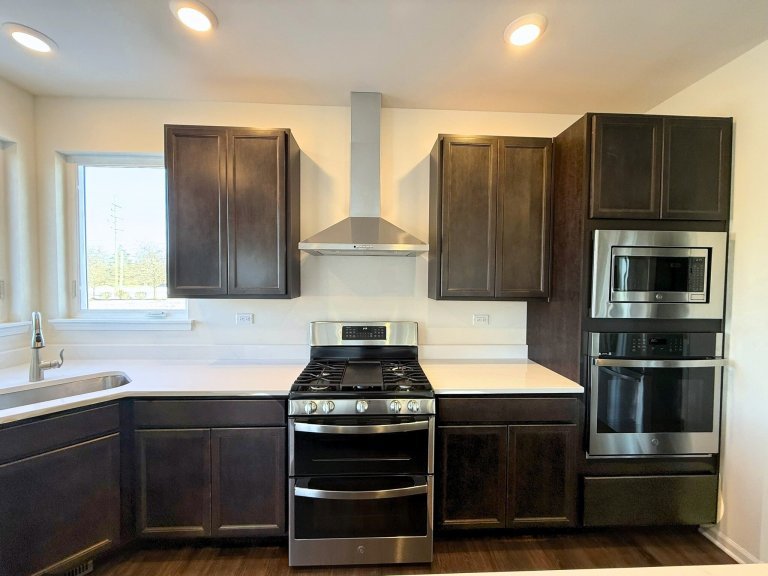 Georgian floor plan kitchen with stainless steel gas range, vent hood, built-in wall oven and microwave, dark cabinetry, and white countertops in a new construction home.”