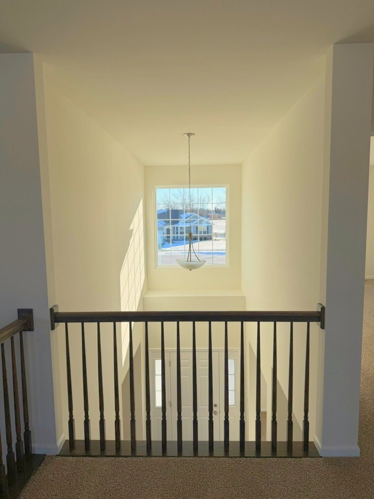 Upper-level overlook to foyer with large picture window, modern chandelier, and open stair railing in a two-story model home.
