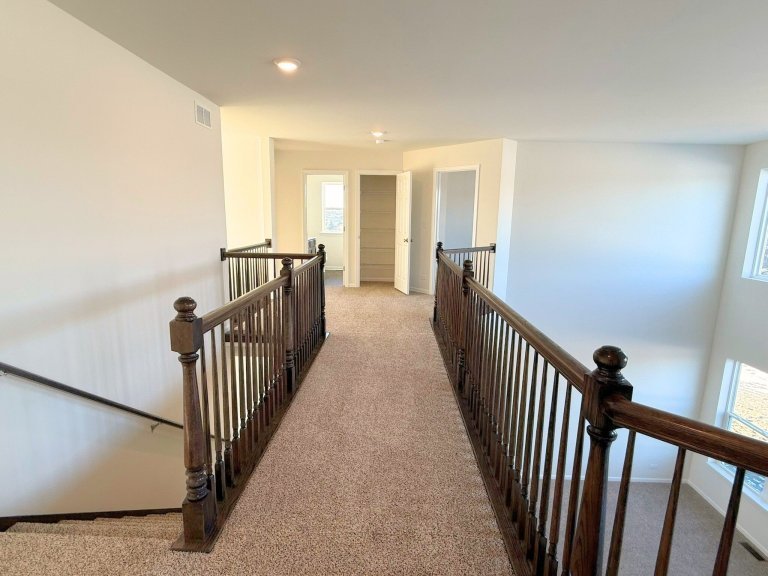 Second-floor loft hallway in Georgian floor plan featuring open railing, neutral carpet, and views to lower level in a modern new construction home.”