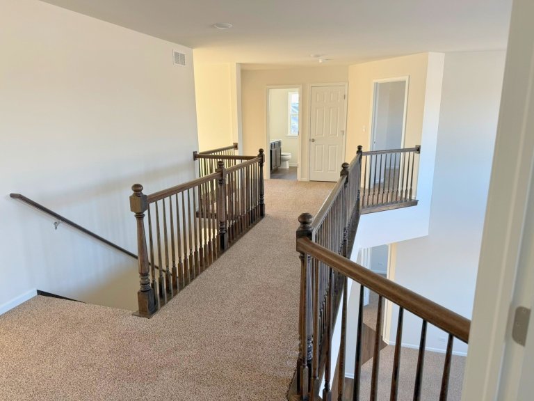 Second-floor loft hallway in Georgian floor plan featuring open railing, neutral carpet, and views to lower level in a modern new construction home.”